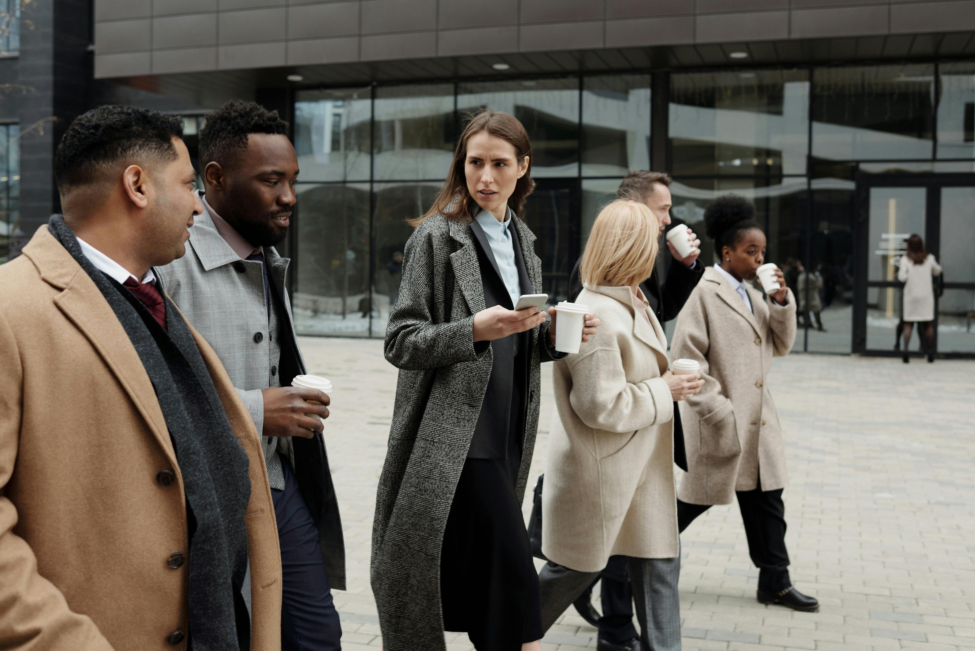 Group of people in winter coats standing outside a building, holding coffee cups.